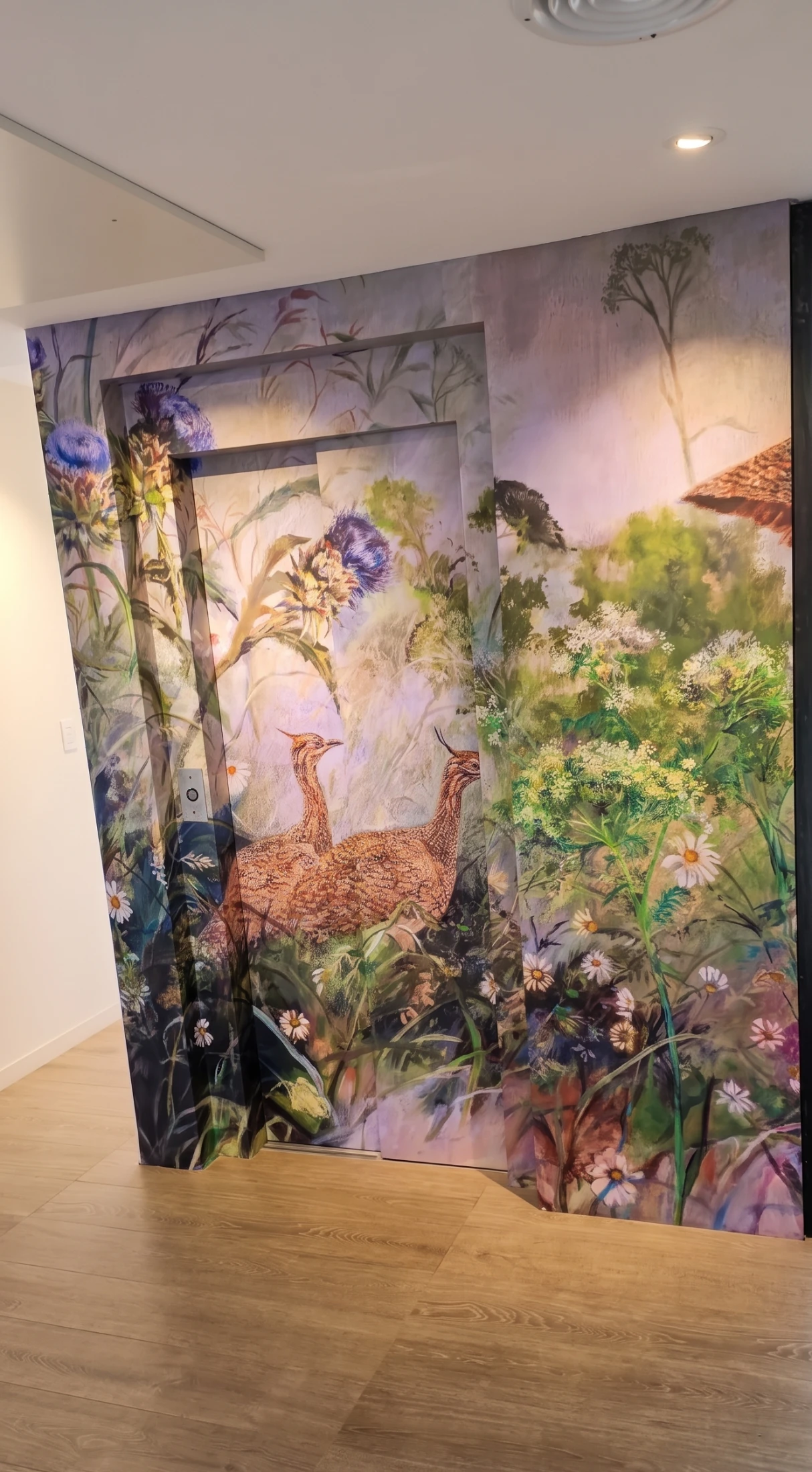 Puertas de ascensor con mural de martinetas y flores silvestres en una vivienda